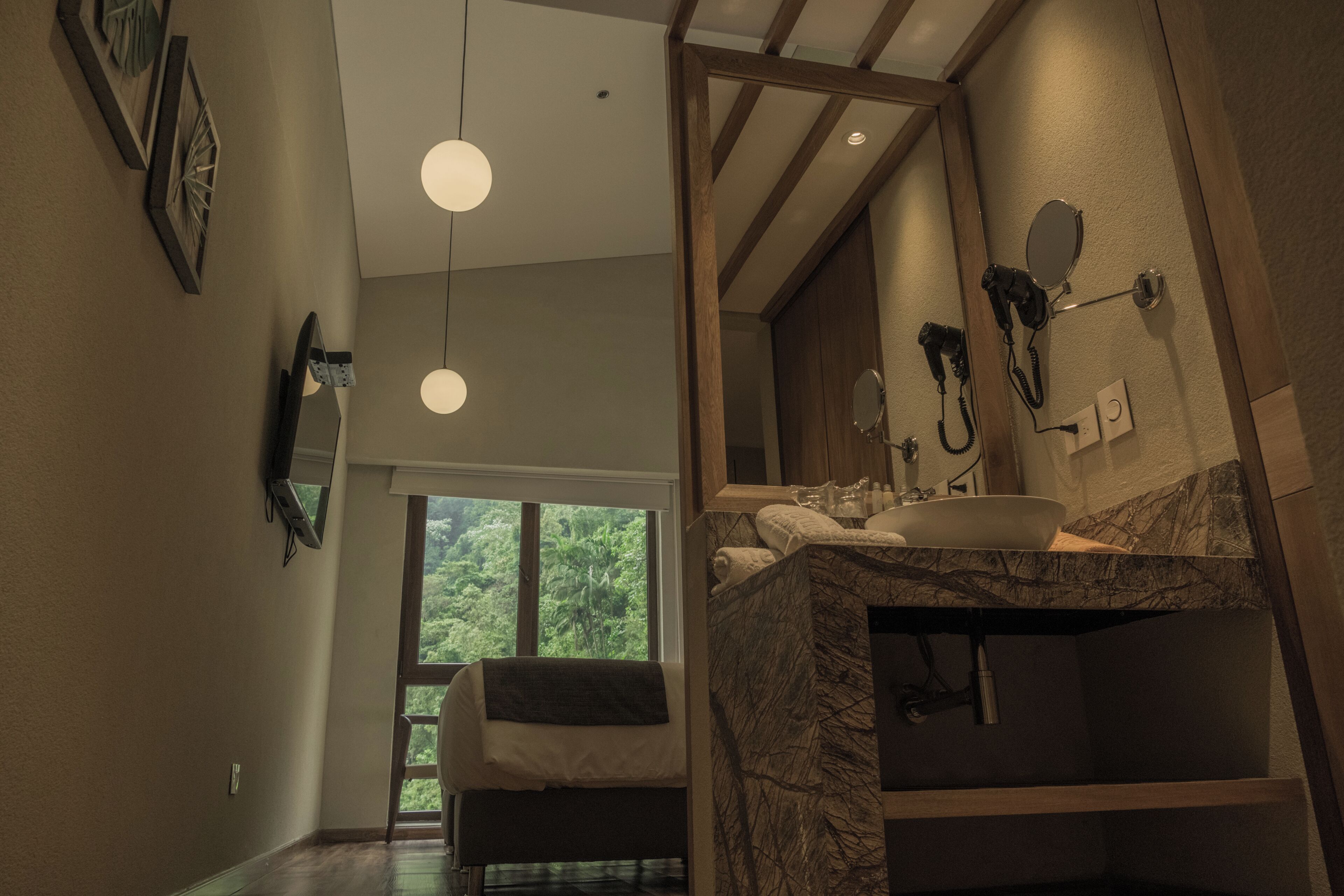 Un baño moderno con un espejo grande, un lavamanos y un secador de pelo. Cuenta con una ventana que proporciona luz natural y vistas al exterior.