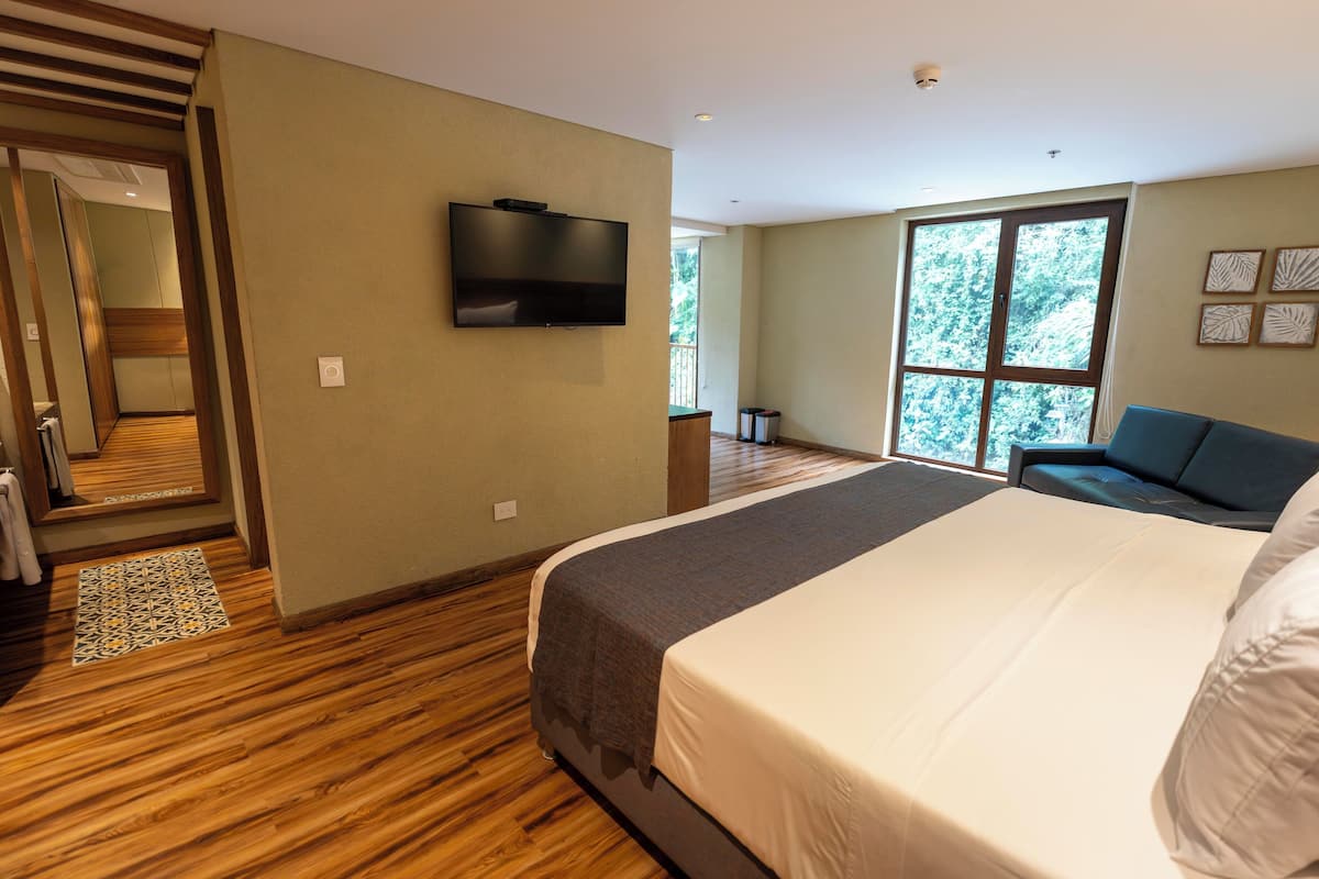Ein modernes Hotelzimmer mit einem großen Bett, einem flachbildfernseher an der Wand und Blick ins Freie durch ein großes Fenster.