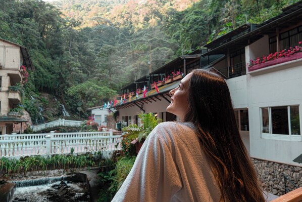 Una persona observa un paisaje montañoso con un edificio que tiene balcones adornados con flores rojas.