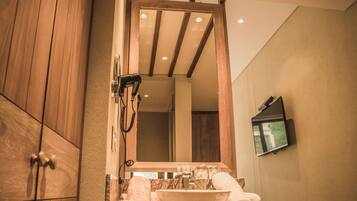 Un baño con tocador de madera, un espejo grande, un lavamanos y un televisor montado en la pared.