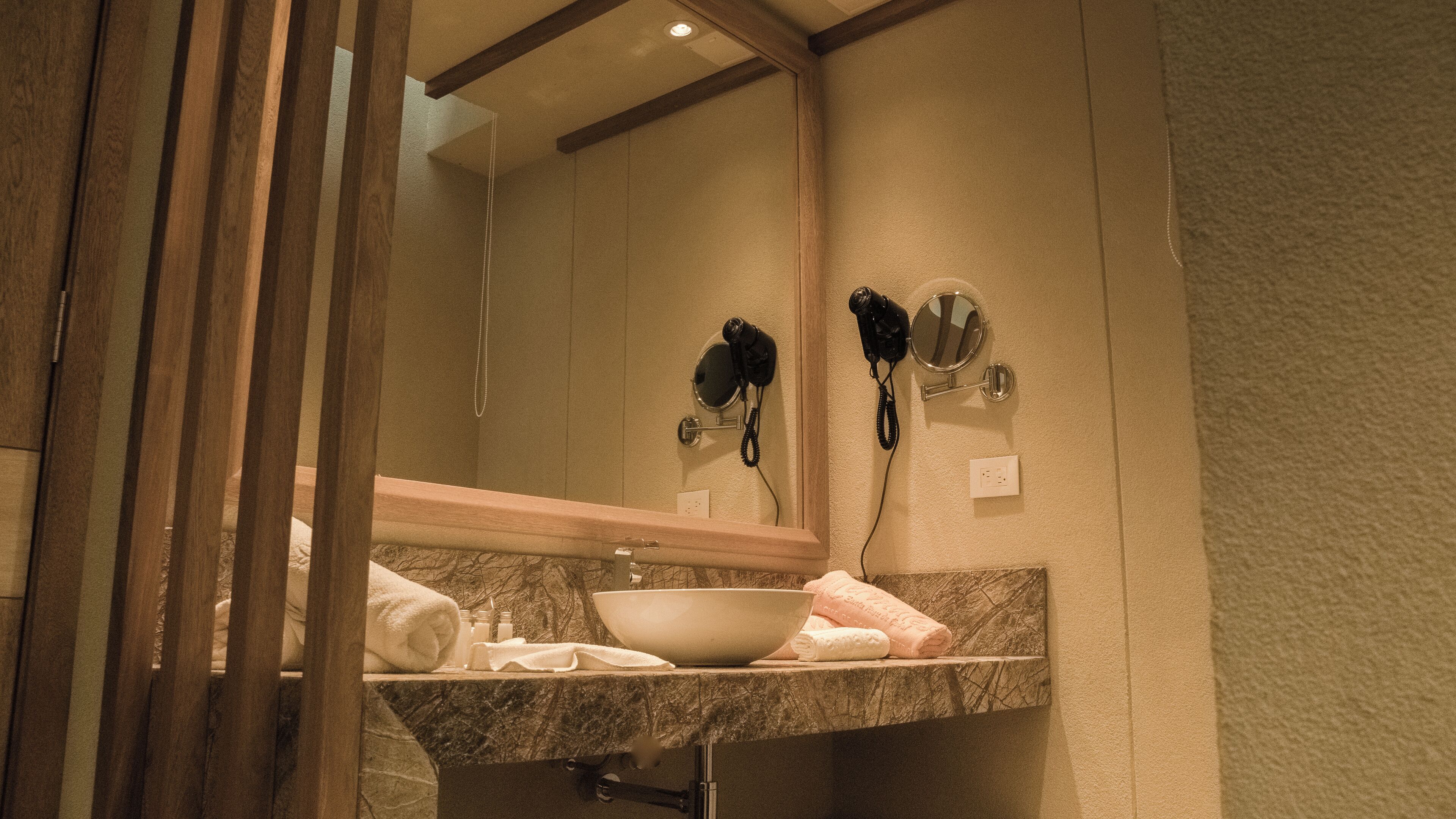 A bathroom with a marble countertop, a sink, a mirror, and two hair dryers mounted on the wall.