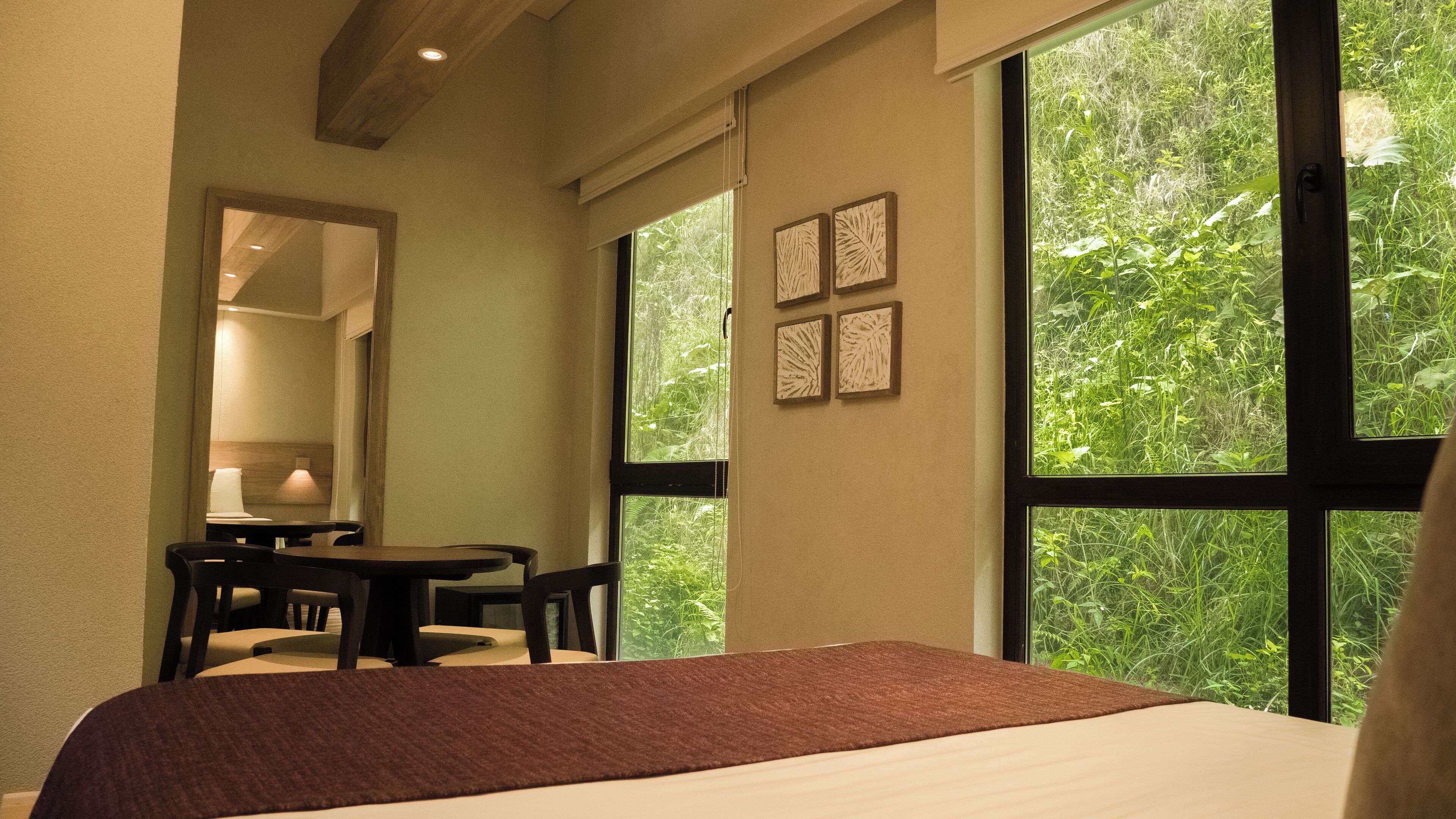 A bedroom with a large bed, a desk, and chairs. There are four framed pictures on the wall.