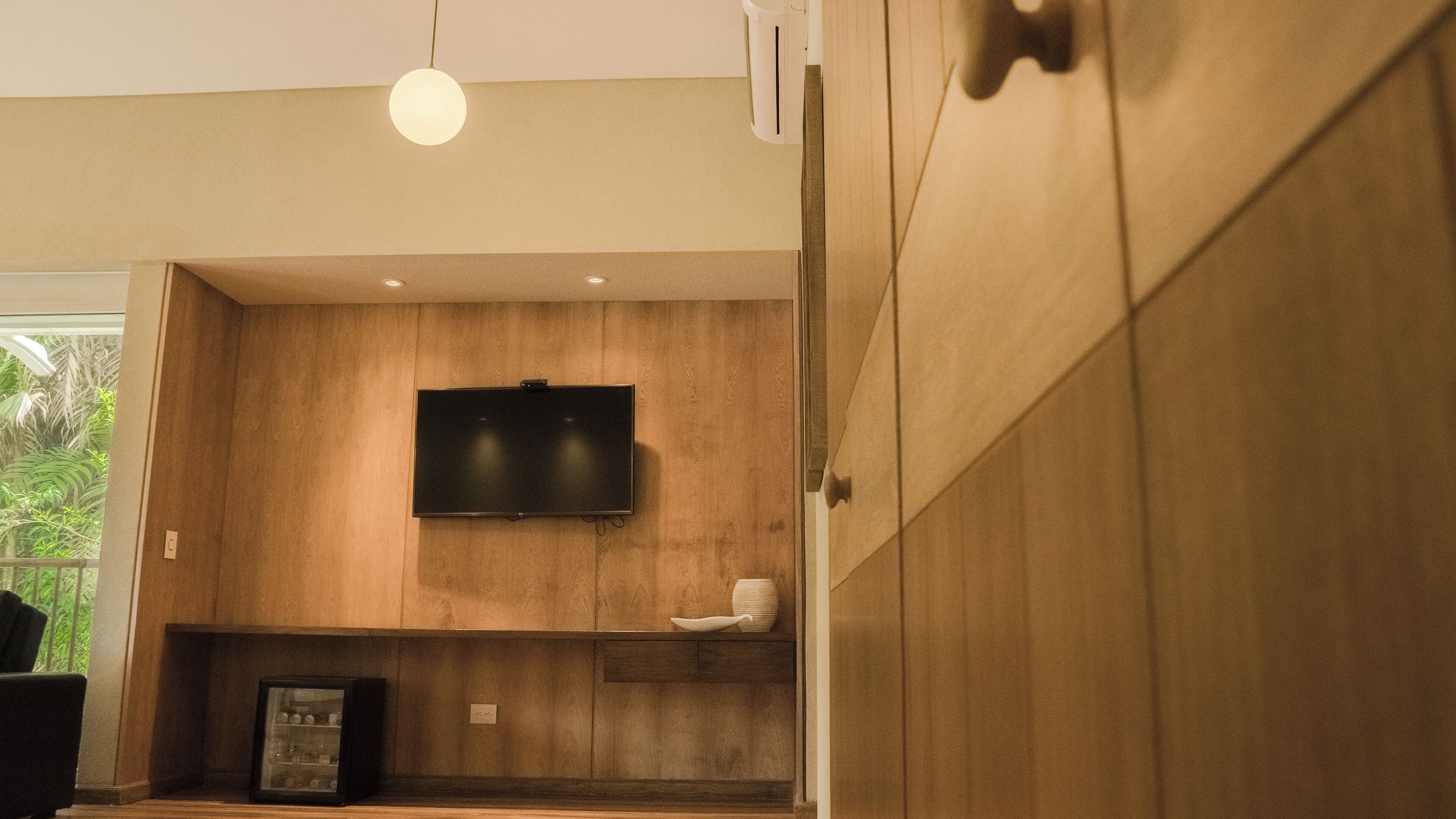 A modern interior with a wooden panel wall, a mounted flat-screen TV, and a pendant light.
