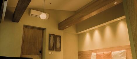A hotel room with a bed, a wooden door, a wall-mounted air conditioner, and a ceiling light fixture.