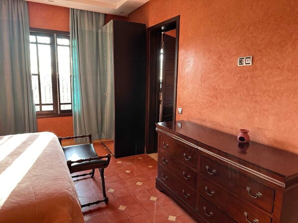 A bedroom with a bed, a wooden bench, a dresser, and a door leading to another room.