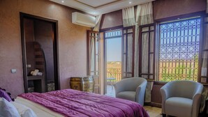 A bedroom with a bed, two chairs, a small table, an air conditioning unit, and a window with a view. - La Terra Rosa (Ghmate)
