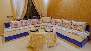 A corner sofa with floral cushions, a matching table, and a window with curtains. - La Terra Rosa (Ghmate)