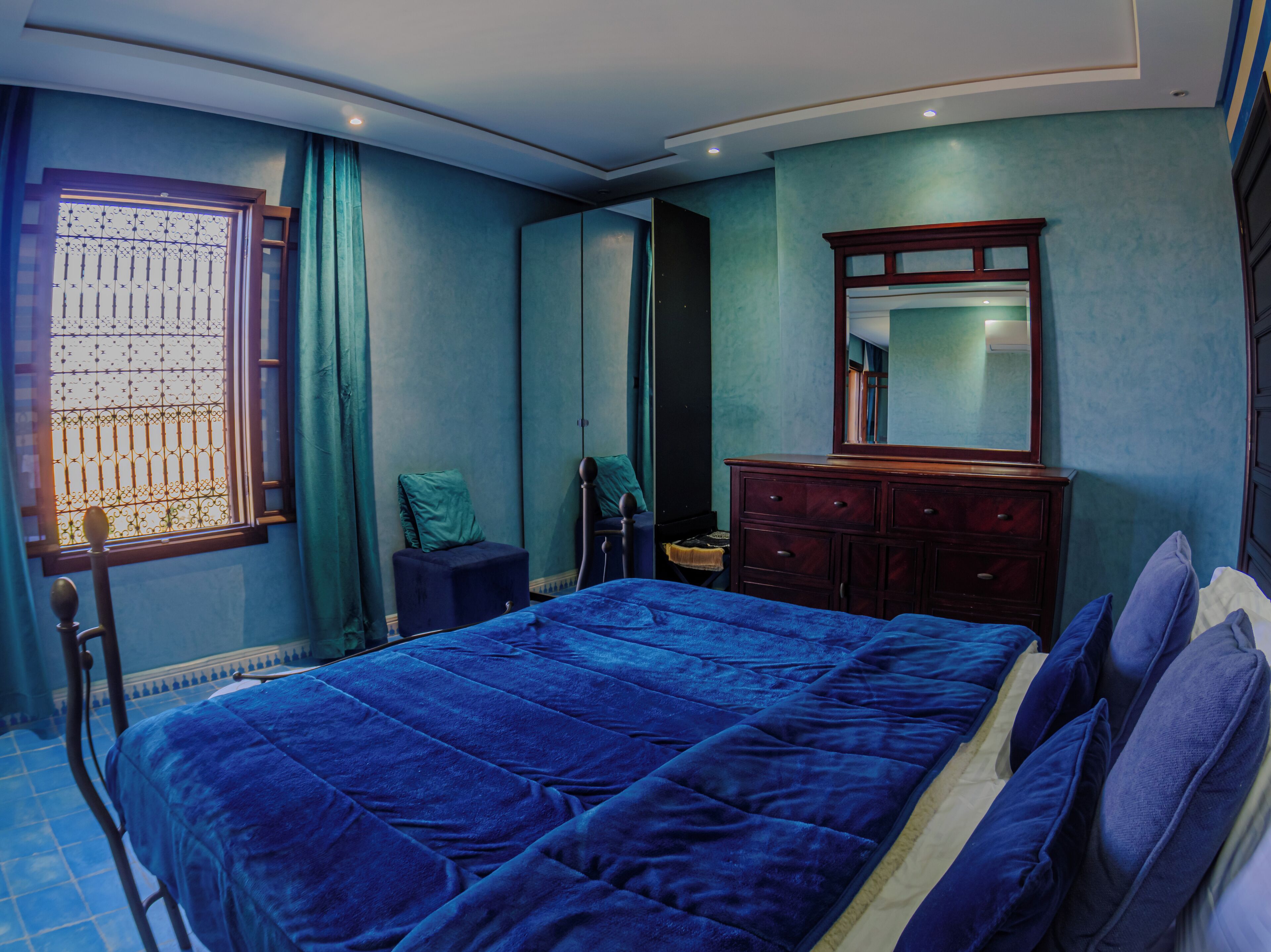 A bedroom with a large bed, a dresser, a mirror, and a window with curtains.
