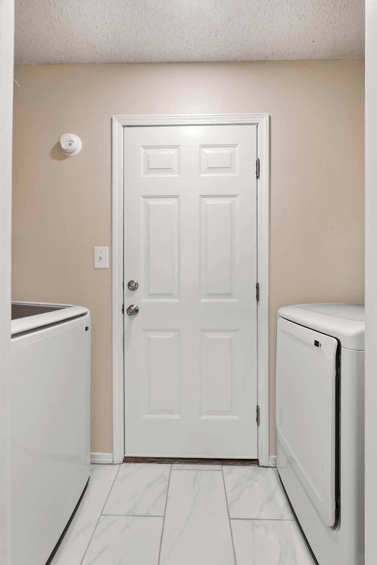 Un cuarto de lavandería con una puerta blanca, dos lavadoras y un calentador instalado en la pared.