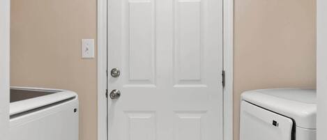 Un cuarto de lavandería con una puerta blanca, dos lavadoras y un calentador instalado en la pared.