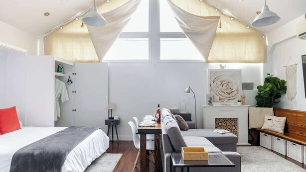 Ein modernes Schlafzimmer mit Bett, Sofa, Esstisch und Kamin.