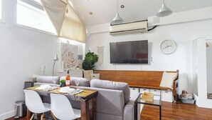 Ein modernes Wohnzimmer mit Sofa, Esstisch, Stühlen, einem Fernseher und einer Klimaanlage.