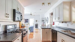 Una cocina con gabinetes blancos, estufa, horno microondas y lavavajillas.