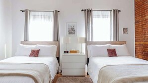 Habitación doble con dos camas, una mesita de noche, una lámpara y un cuadro en la pared.