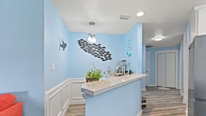 Una cocina con pared azul claro, encimera de mármol y refrigerador de acero inoxidable.