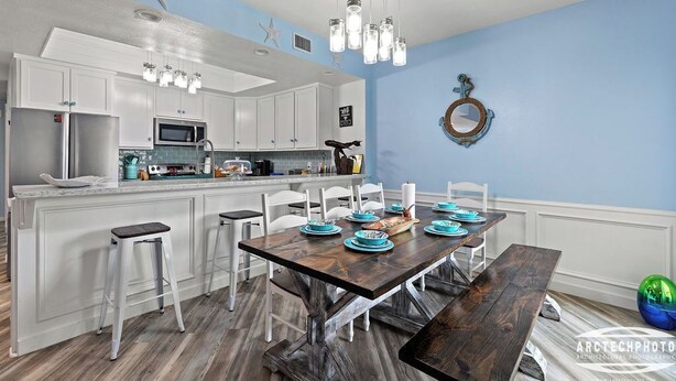 Una cocina moderna con armarios blancos, una isla central y un área de comedor con mesa y sillas de madera.