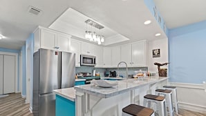 Cocina moderna con armarios blancos, electrodomésticos de acero inoxidable, una pared de acento azul y una isla central con taburetes de bar.