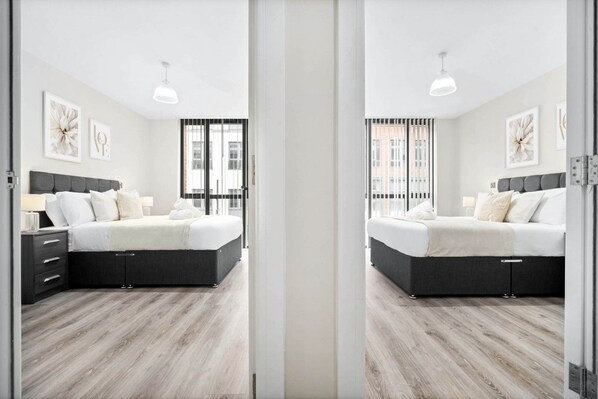 A modern bedroom with a large bed, a nightstand, and a window with blinds.