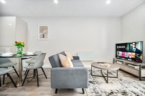 A modern living room with a grey sofa, a glass dining table, and a flat-screen TV displaying Netflix content. - Stylish 2 Bed Apartment - Smart TV - WIFI -  Jewellery Quarter 1 (Birmingham)