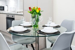 A modern dining area with a glass table set for four, surrounded by grey chairs. - Stylish 2 Bed Apartment - Smart TV - WIFI -  Jewellery Quarter 1 (Birmingham)