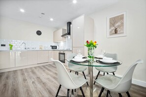 Cozinha moderna com armários brancos, uma mesa de jantar de vidro e um vaso com flores.