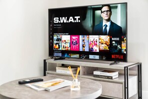 A television displaying the show S.W.A.T. on Netflix, with a remote control and books on a side table.
