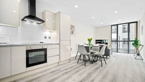 A modern kitchen with white cabinetry, a black range hood, and a dining area with a table and chairs. - Luxury 2 Bed Apartment - Smart TV - WIFI (Birmingham)