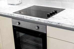 A kitchen with a built-in induction cooktop, a stainless steel oven, and a marble countertop.