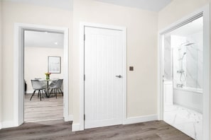 A hallway with a dining area, a white door, and a shower area with marble tiles.