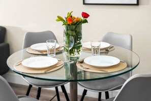 A round glass table with four white plates, each with a gold placemat, and a clear glass vase with flowers in the center. - Luxury 2 Bed Apartment - Smart TV - WIFI -  Jewellery Quarter (Birmingham)