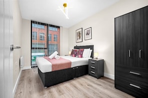 A modern bedroom with a bed, bedside table, wardrobe, and a view of a building through a window. - Stylish 2 Bed Apartment - Smart TV - WIFI -  Jewellery Quarter (Birmingham)