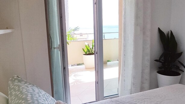 A bedroom with a bed, a window with curtains, a view of the outdoors, and a potted plant. - Apartment Ana with sea view - Two Bedroom Apartment with Terrace and Sea View (Crikvenica)