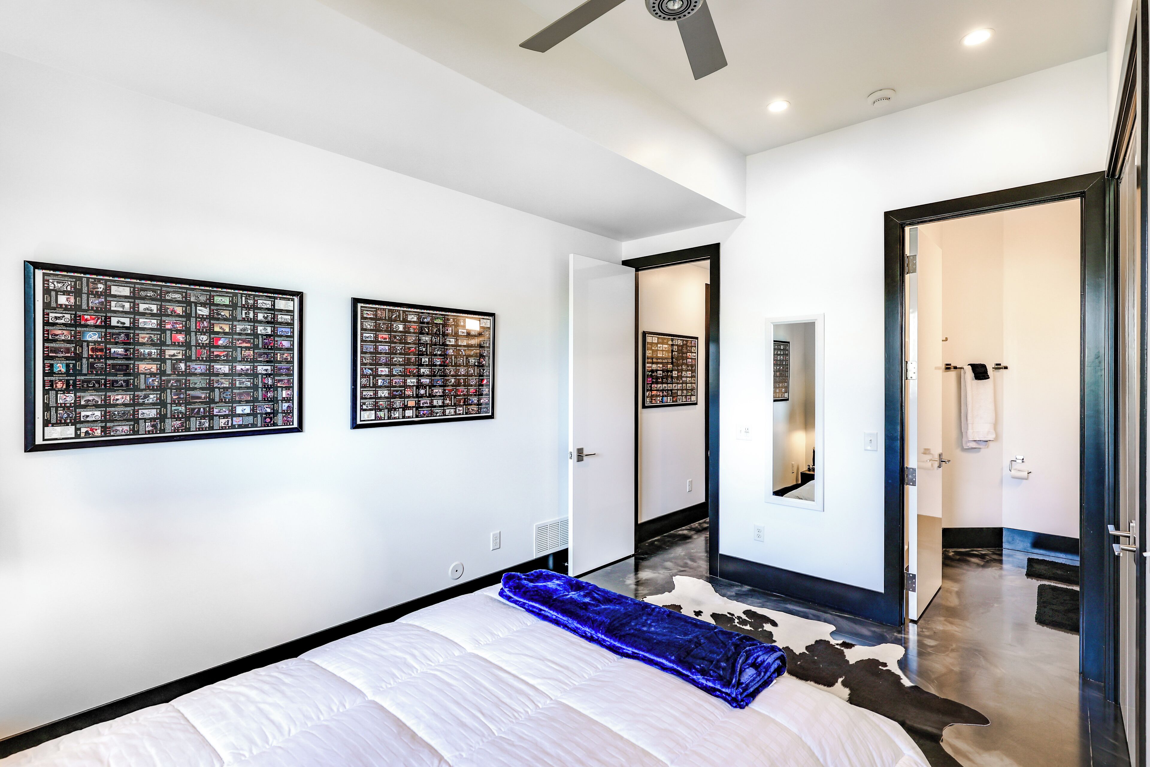 A modern hotel room with a large bed, a ceiling fan, and two framed pictures on the wall.