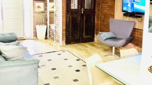 Una sala de estar con televisor, sofá, sillón y mesa de comedor.