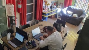 A room with a dining table, two laptops, a television, and a sofa. - Hostel Dumah (São Paulo)
