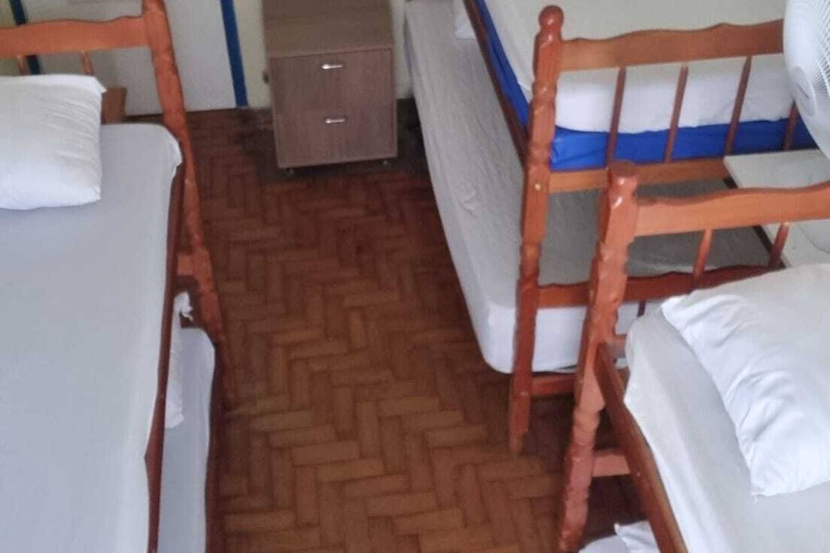 Ein kleiner, schlichter Raum mit zwei Holzbetten, einem kleinen Holzschrank und einem weißen Wandventilator.