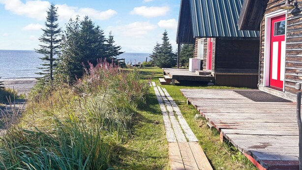 A wooden cabin with a red door, a metal roof, and a wooden deck leading to the entrance.