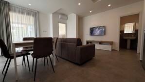 Ein modernes Wohnzimmer mit Essbereich, einer Couch, einem Fernseher und einem durchgegangenen Tür erkennbaren Badezimmer.