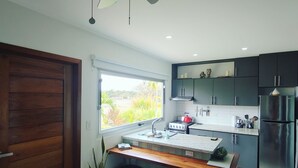 A modern kitchen with a central island, a ceiling fan, and a view of the outdoors through a window.