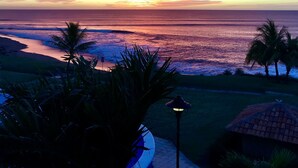 A sunset view over the ocean with palm trees and a lamp post in the foreground.