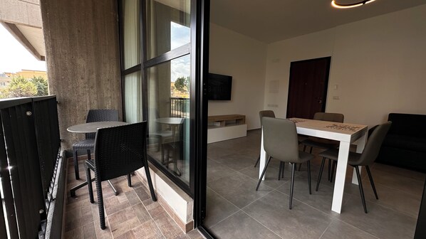 Un comedor moderno con pared de vidrio, televisor montado en la pared y sofá de color oscuro.