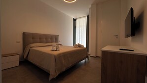 Moderni hotellihuone, jossa on suuri sänky, puinen yöpöytä, seinälle asennettu taulutelevisio ja ikkuna, jossa on läpikuultavat verhot.