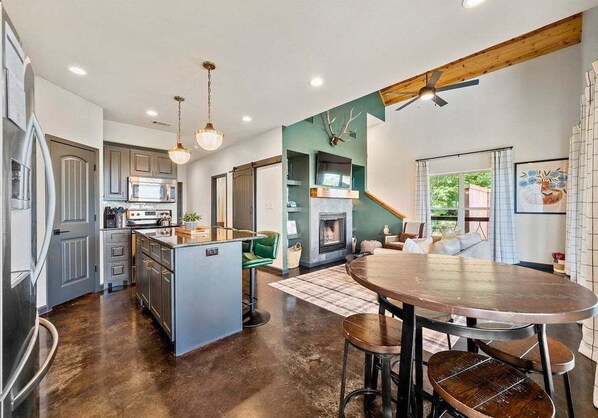 A modern kitchen with a central island, a dining area with a round table, and a fireplace.
