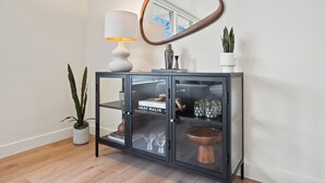 A black cabinet with glass doors, a white lamp, a round mirror, and a potted plant. - Yard w/ fire pit & grill, king bed, light filled (Boise)