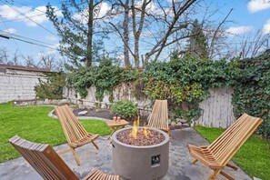 A backyard with a fire pit, wooden chairs, and a small table. - Yard w/ fire pit & grill, king bed, light filled (Boise)