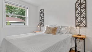 Un dormitorio con cama, dos mesitas de noche, una ventana y decoración en la pared.