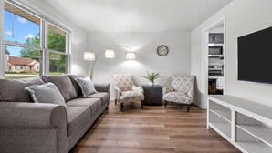 Una sala de estar con un sofá gris, sillones estampados, un aparador y un televisor grande.