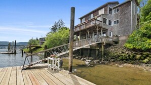 A wooden dock leading to a house with a balcony, surrounded by greenery and a body of water. - *Riverfront*Pvt Dock*Game Room*6 mins to Beach* (Nehalem)