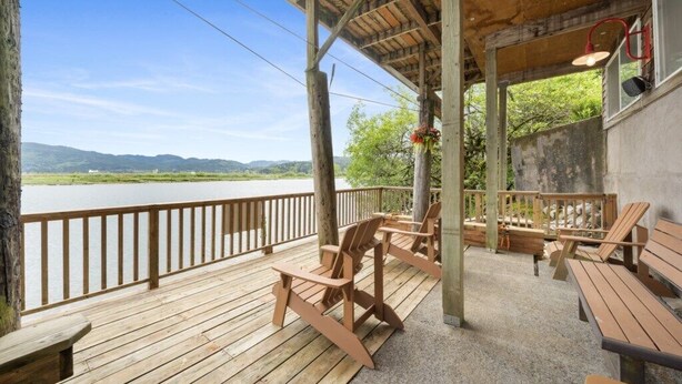 A wooden deck with chairs and tables overlooking a body of water and hills. - *Riverfront*Pvt Dock*Game Room*6 mins to Beach* (Nehalem)