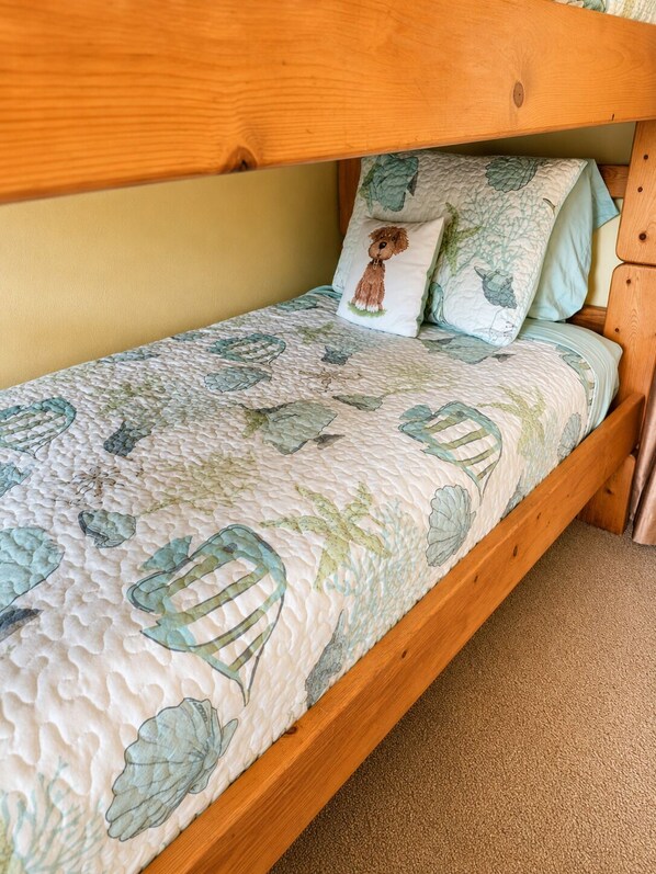 A single bed with a quilted mattress featuring a leaf pattern, a wooden headboard, and two pillows with a leaf design.
